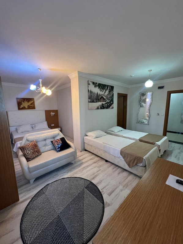 A modern hotel room with a sofa, two beds, a dining table, and a mirror.
