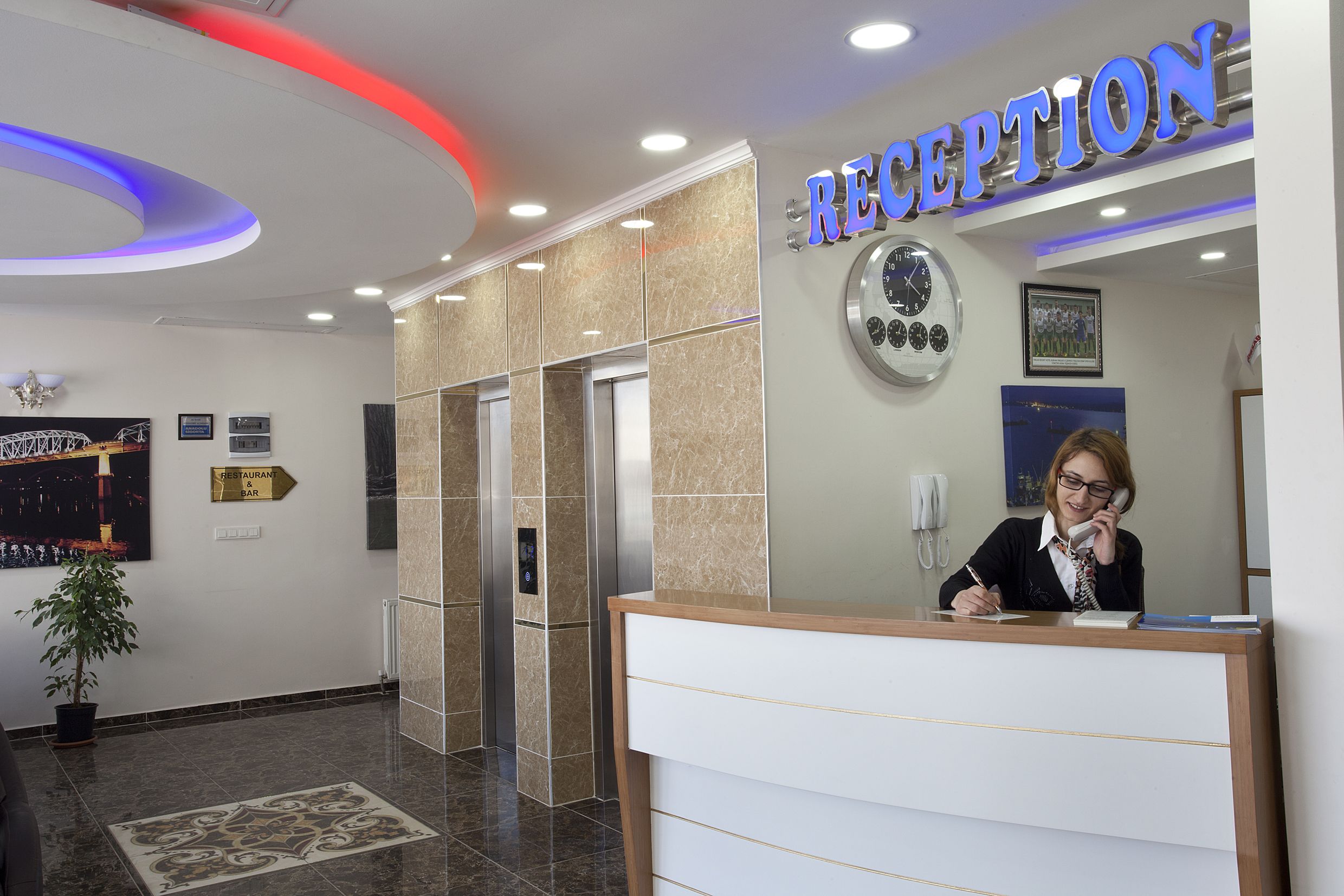 Un área de recepción con mostrador, un reloj y un cartel que indica el camino al restaurante y al bar.