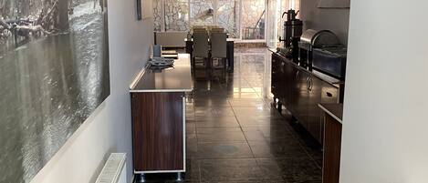 A modern kitchen with a stone backsplash, a dining area with chairs, and a view through large windows.