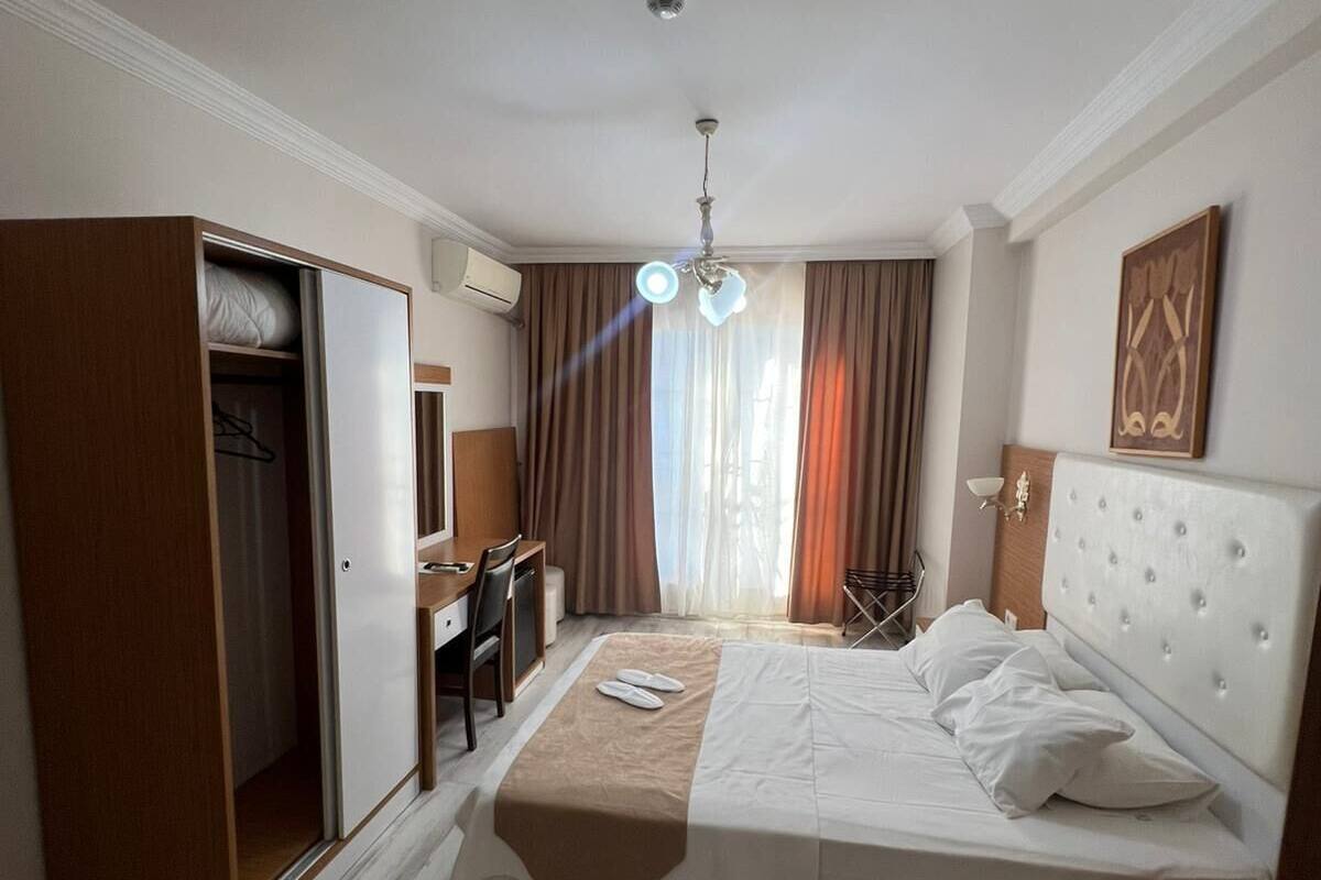 A hotel room with a bed, desk, chair, wardrobe, and a ceiling light.