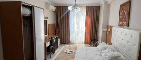 Hotellihuone, jossa on sänky, työpöytä, tuoli, vaatekaappi ja kattovalaisin.