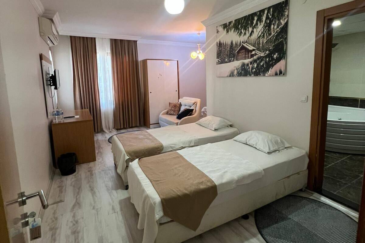 A hotel room with two beds, a desk, a chair, a painting, and a view of the outside.
