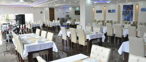 A spacious dining area with multiple tables set for service, a stage with musical equipment, and a modern ceiling design.