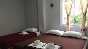 A hotel room with two single beds, each with a red bedspread and white pillows. There are two towels placed on the beds.