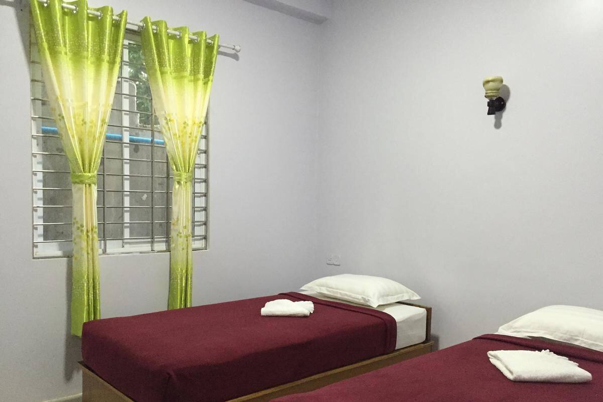 Une chambre avec deux lits simples, chacun recouvert d’une courtepointe rouge et agrémenté d’oreillers blancs, et une fenêtre avec des rideaux verts.