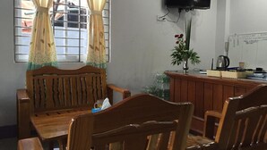 A room with a wooden dining table and chairs, a television mounted on the wall, and a window with curtains.