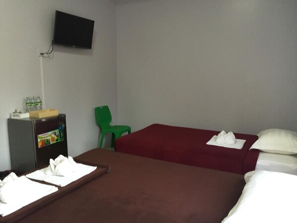 A hotel room with two beds, a TV mounted on the wall, a small desk with a refrigerator, and a green chair.