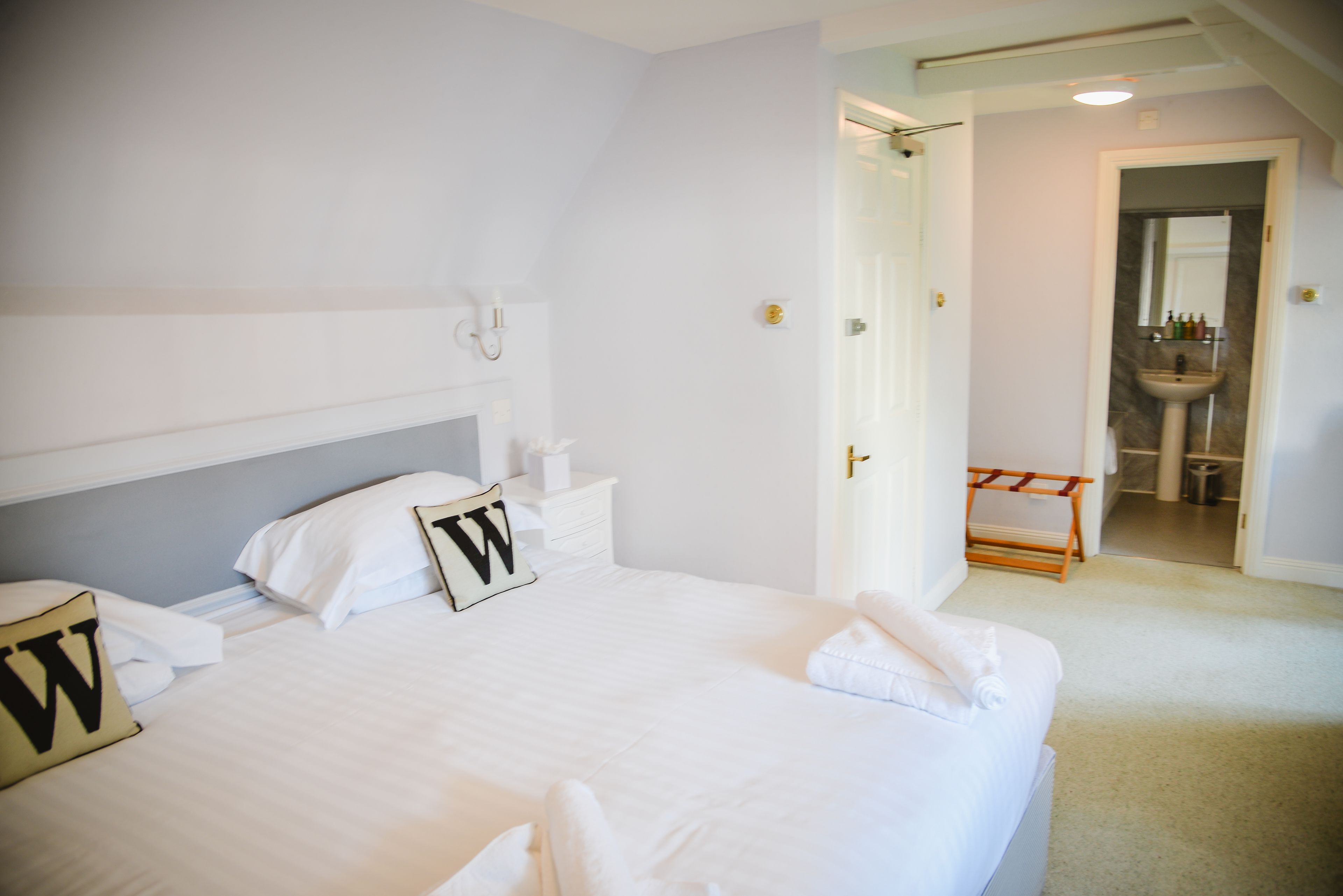 A hotel room with a large bed, a bedside table, a nightstand, a bathroom with a sink, and a mirror.