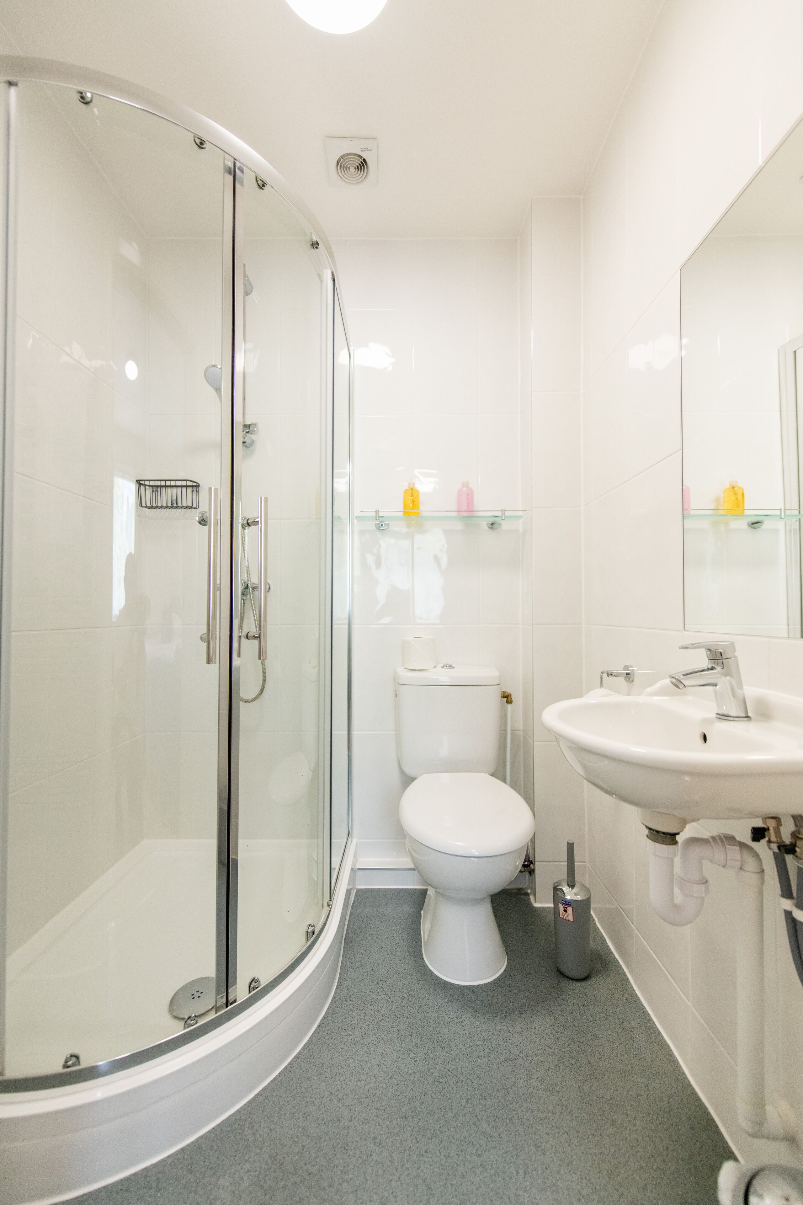 A modern bathroom with a glass-enclosed shower, a white toilet, and a sink with a mirror above it.