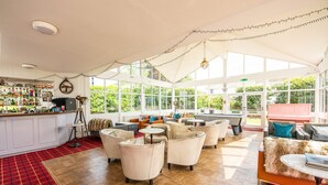 A spacious indoor area with a bar, seating arrangements, and large windows allowing natural light. - Woodlands Hotel (Sidmouth)