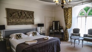 A bedroom with a large bed, a dresser, a mirror, a chair, and a window with curtains. - Woodlands Hotel (Sidmouth)