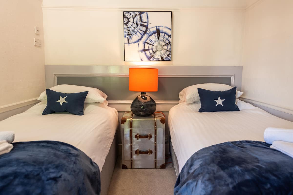 Ett hotellrum med två sängar, var och en med en kudde prydd med ett stjärnmönster, en resväska och en lampa placerad mellan dem.
