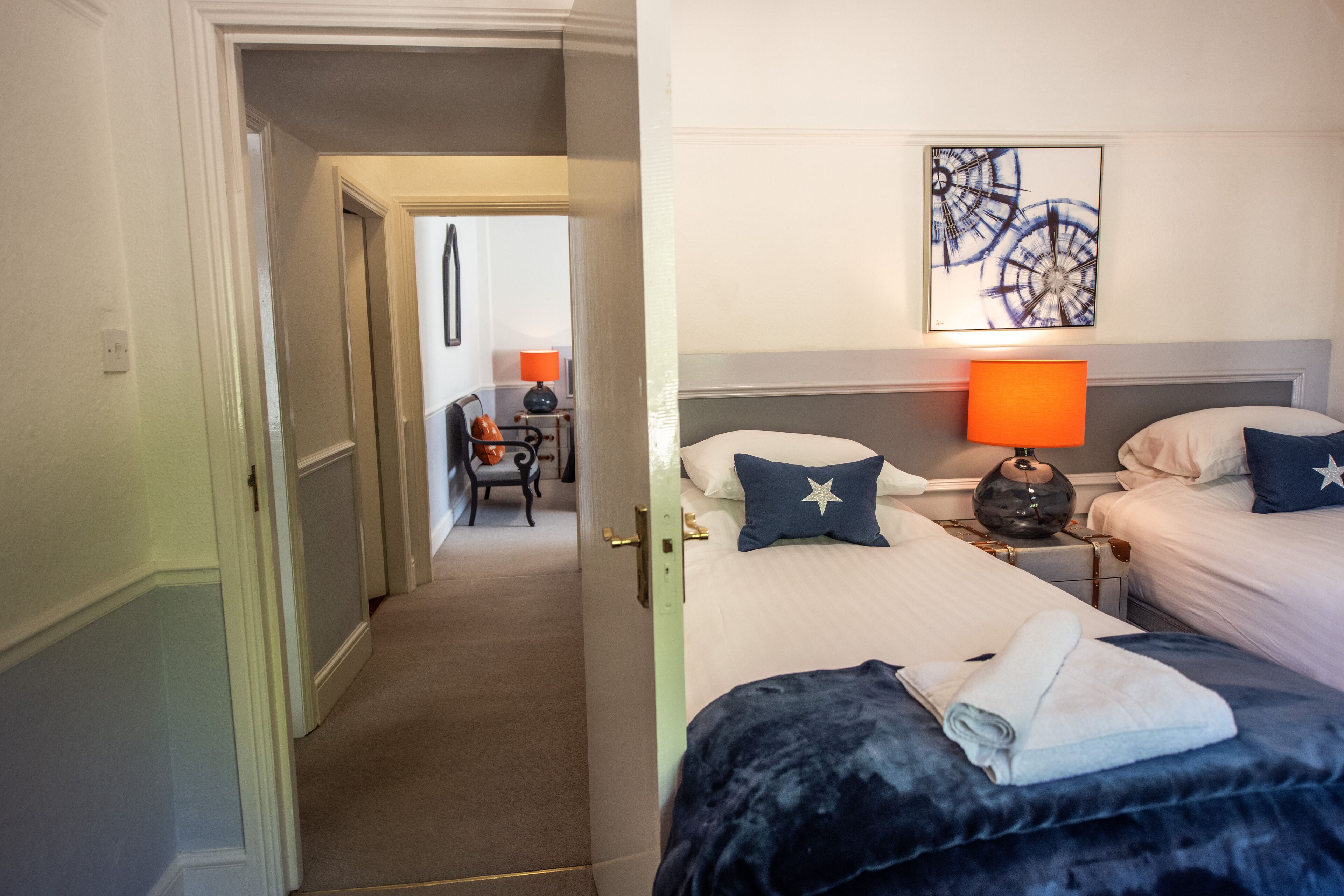 Camera d'albergo con due letti, un comodino con una lampada, una sedia e un quadro appeso al muro.