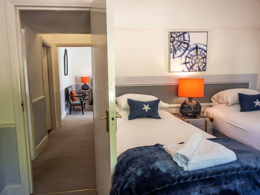 Camera d'albergo con due letti, un comodino con una lampada, una sedia e un quadro appeso al muro.