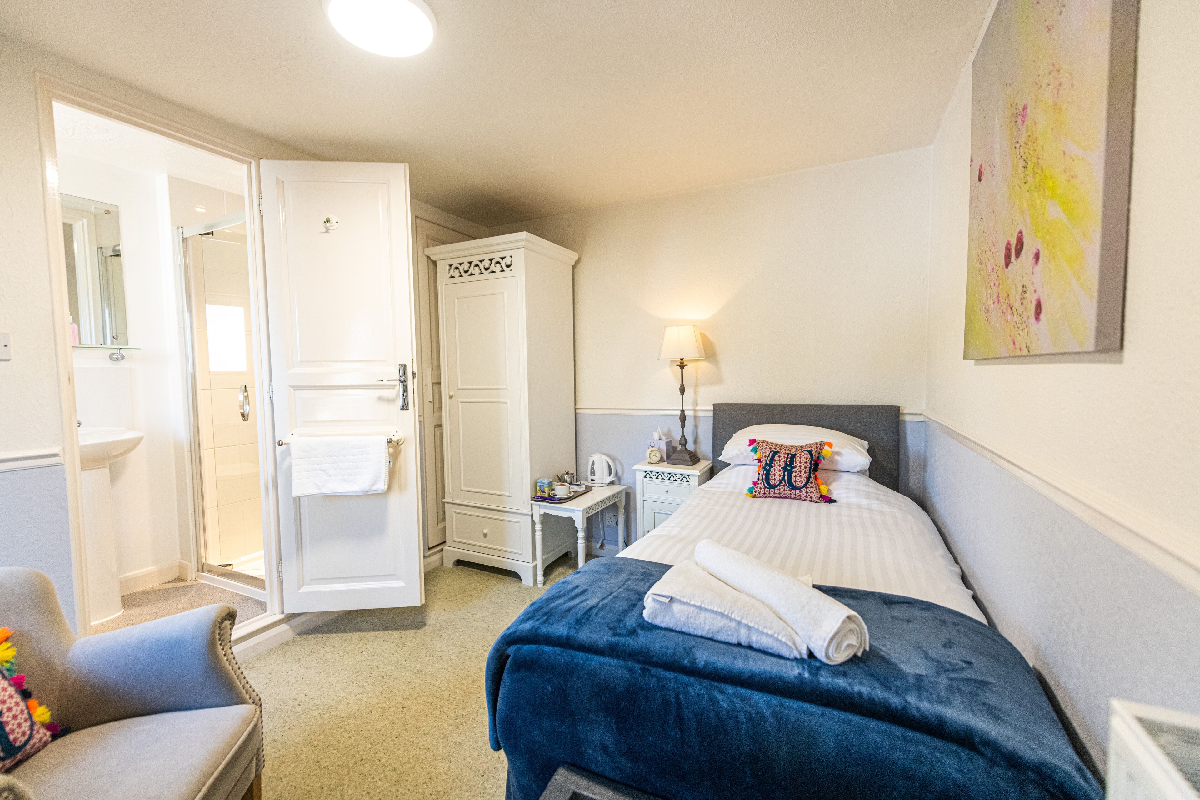 A hotel room with a bed, a chair, a wardrobe, a nightstand, and a lamp.