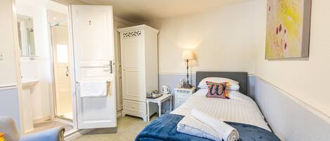 A hotel room with a bed, a chair, a wardrobe, a nightstand, and a lamp.