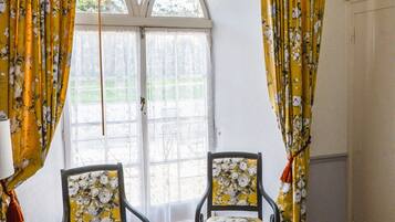 A room with a bed, two chairs, a window with curtains, and a hanging lamp.