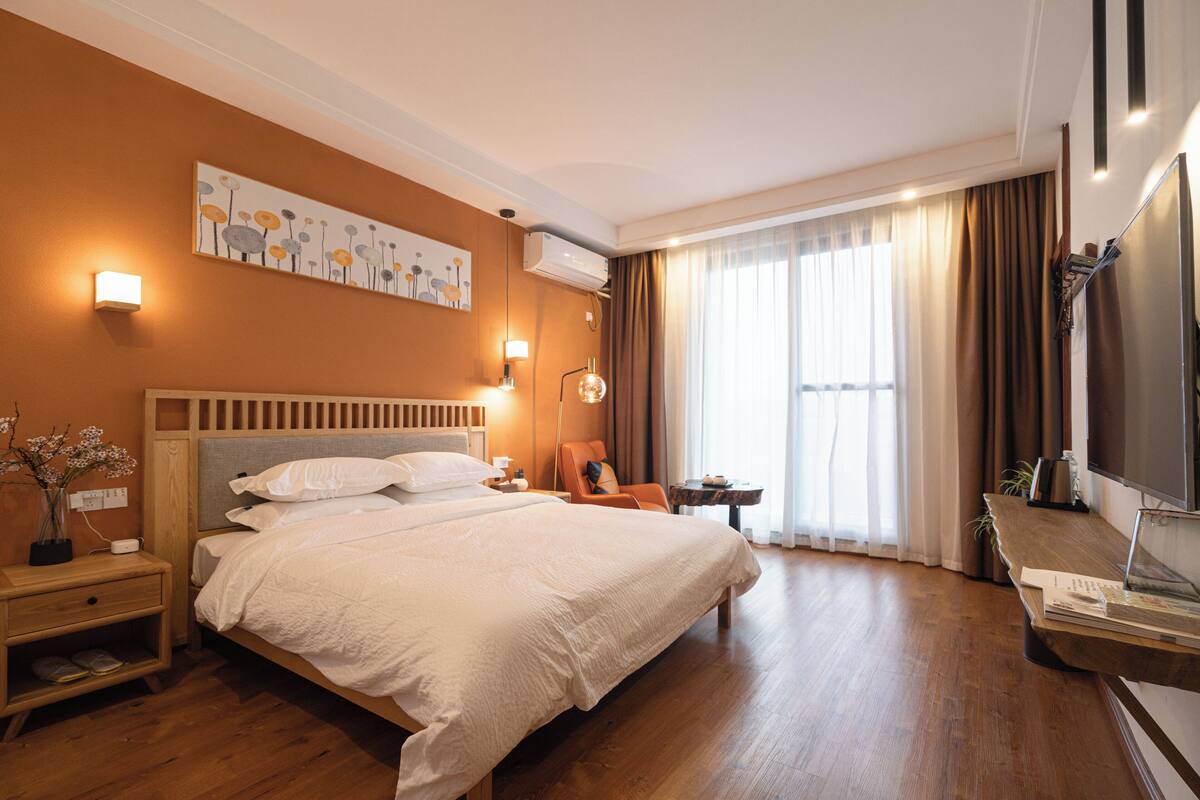 Een hotelkamer met een groot bed, nachtkastjes, een bureau, een televisie en een raam met gordijnen.
