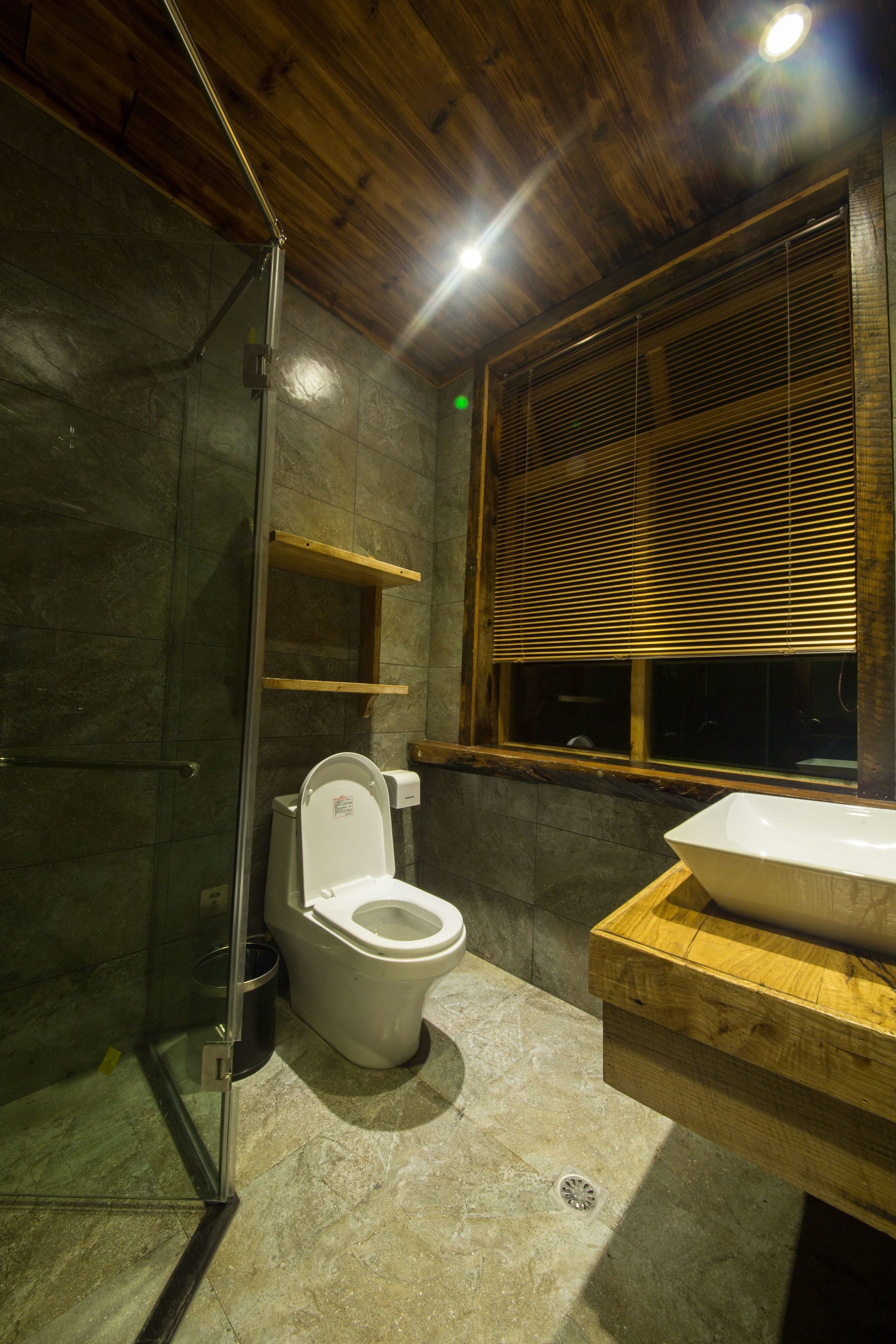 Un bagno con cabina doccia in vetro, un water bianco e un mobile bagno in legno con lavandino.