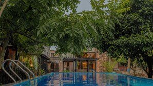 A swimming pool with a stone building in the background. - Tian's Resort (Zhangjiajie)