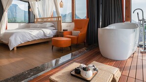 A modern bedroom with a bed, an orange chair, a large bathtub, and a tray with teapots. - Tian's Resort (Zhangjiajie)