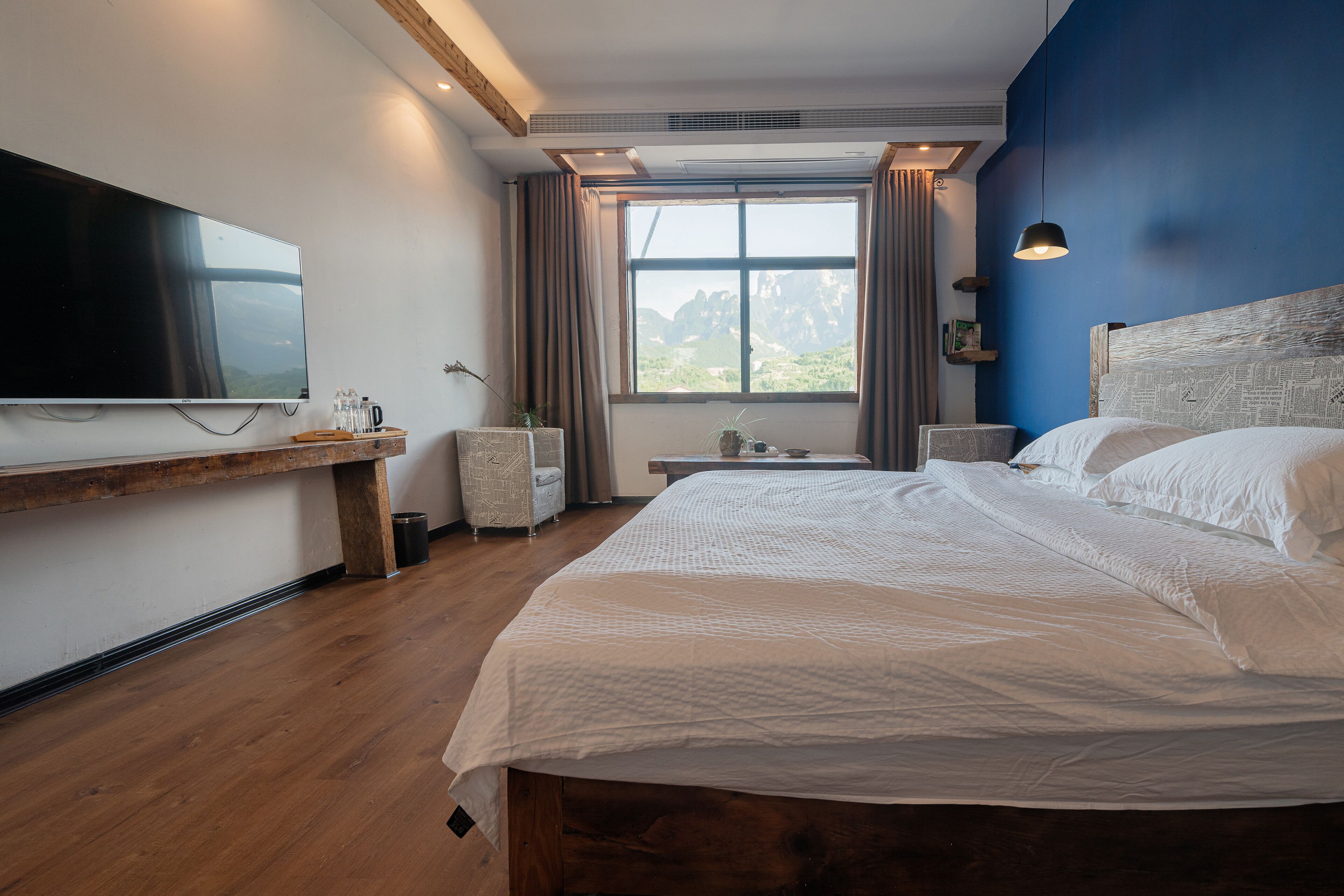 Habitación de hotel moderna con una cama grande, una televisión de pantalla plana, un banco de madera y una ventana con vista a la montaña.