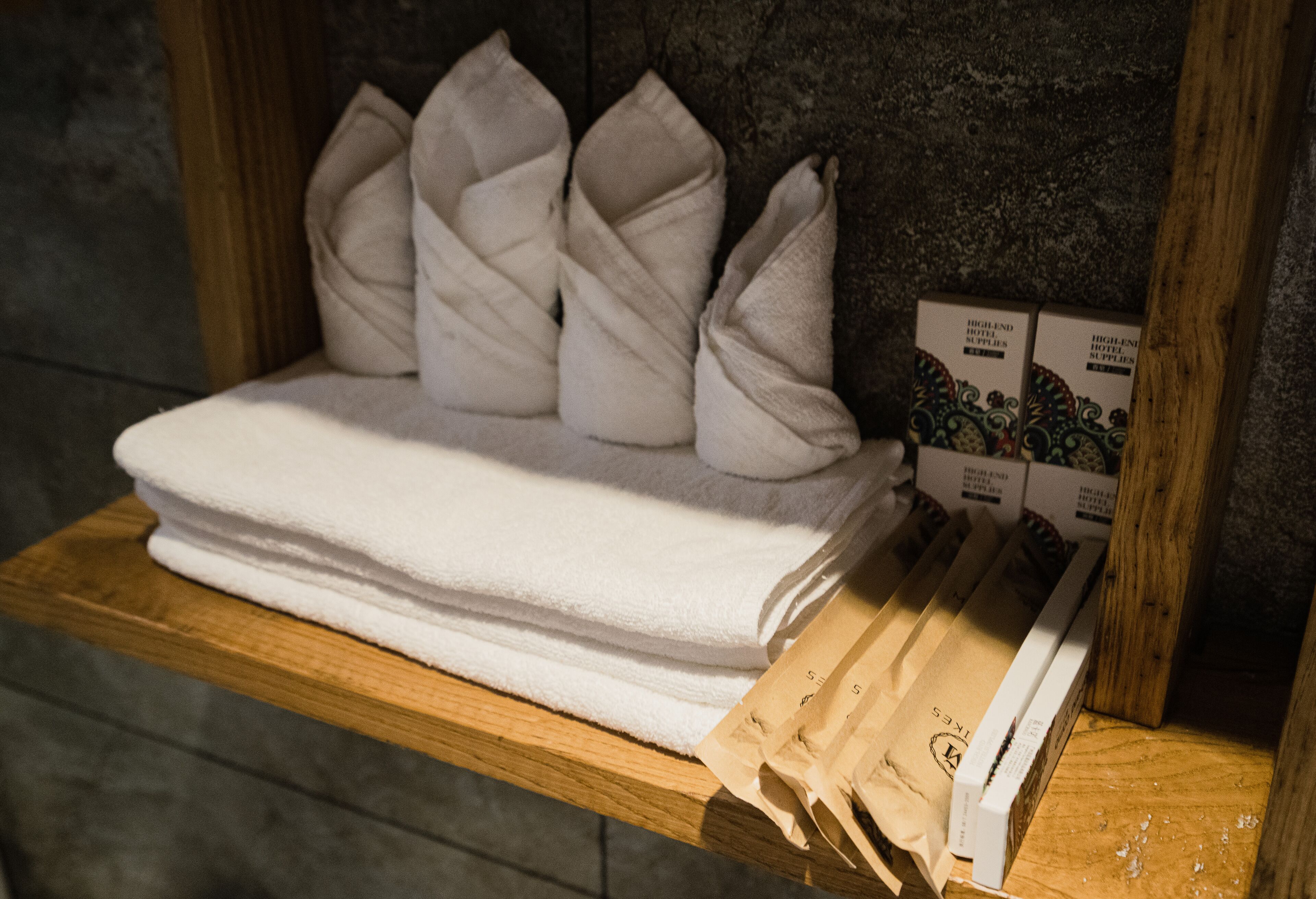 A neatly folded white towel on a wooden shelf, accompanied by a stack of brown paper bags and boxes labeled "Highland Hotel Supplies."