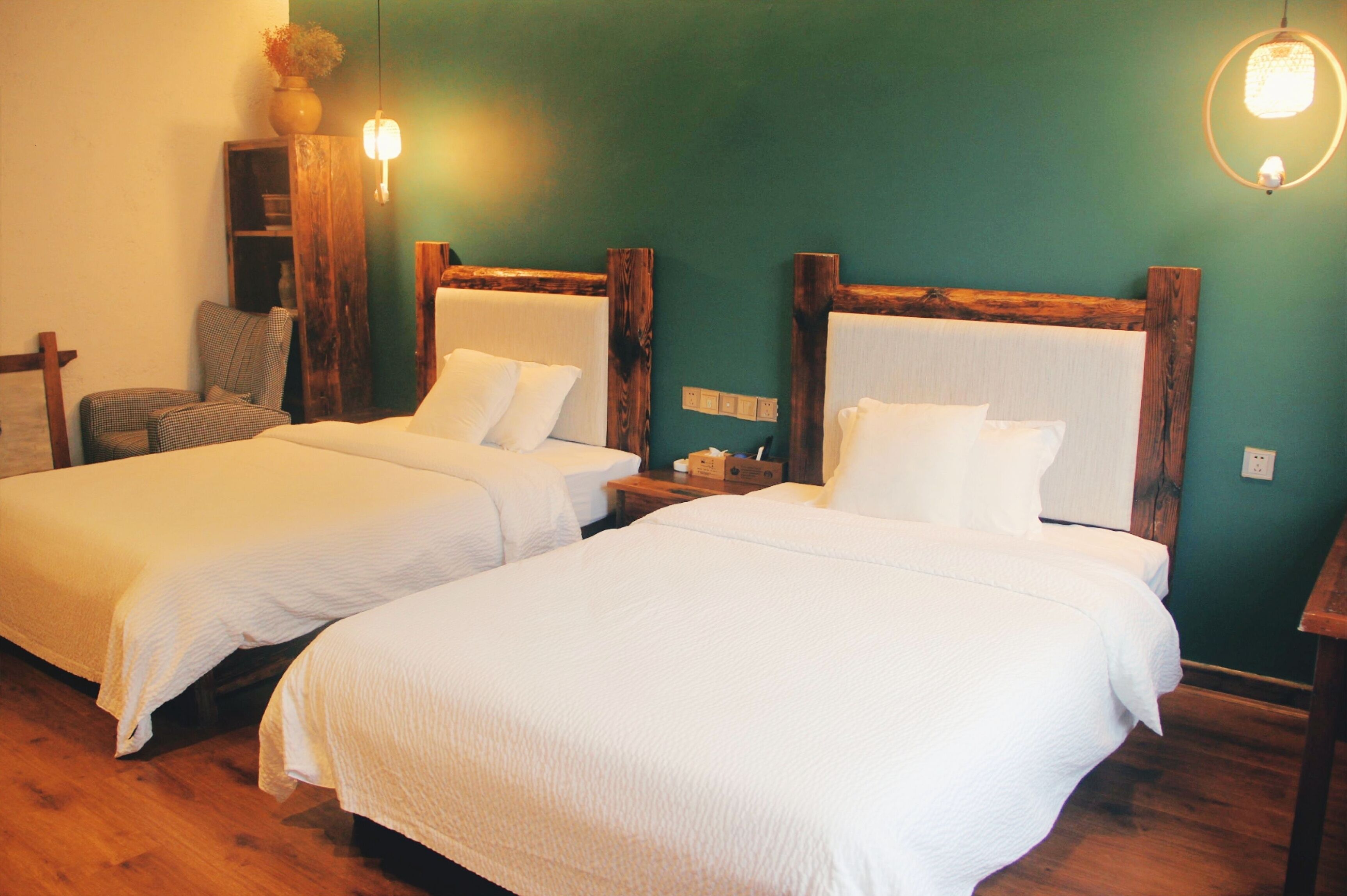 Two single beds with wooden headboards, a small wooden nightstand, a chair, and a wall-mounted shelf with a vase.