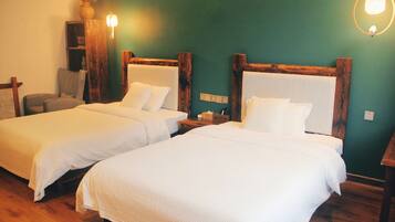 Two single beds with wooden headboards, a small wooden nightstand, a chair, and a wall-mounted shelf with a vase.