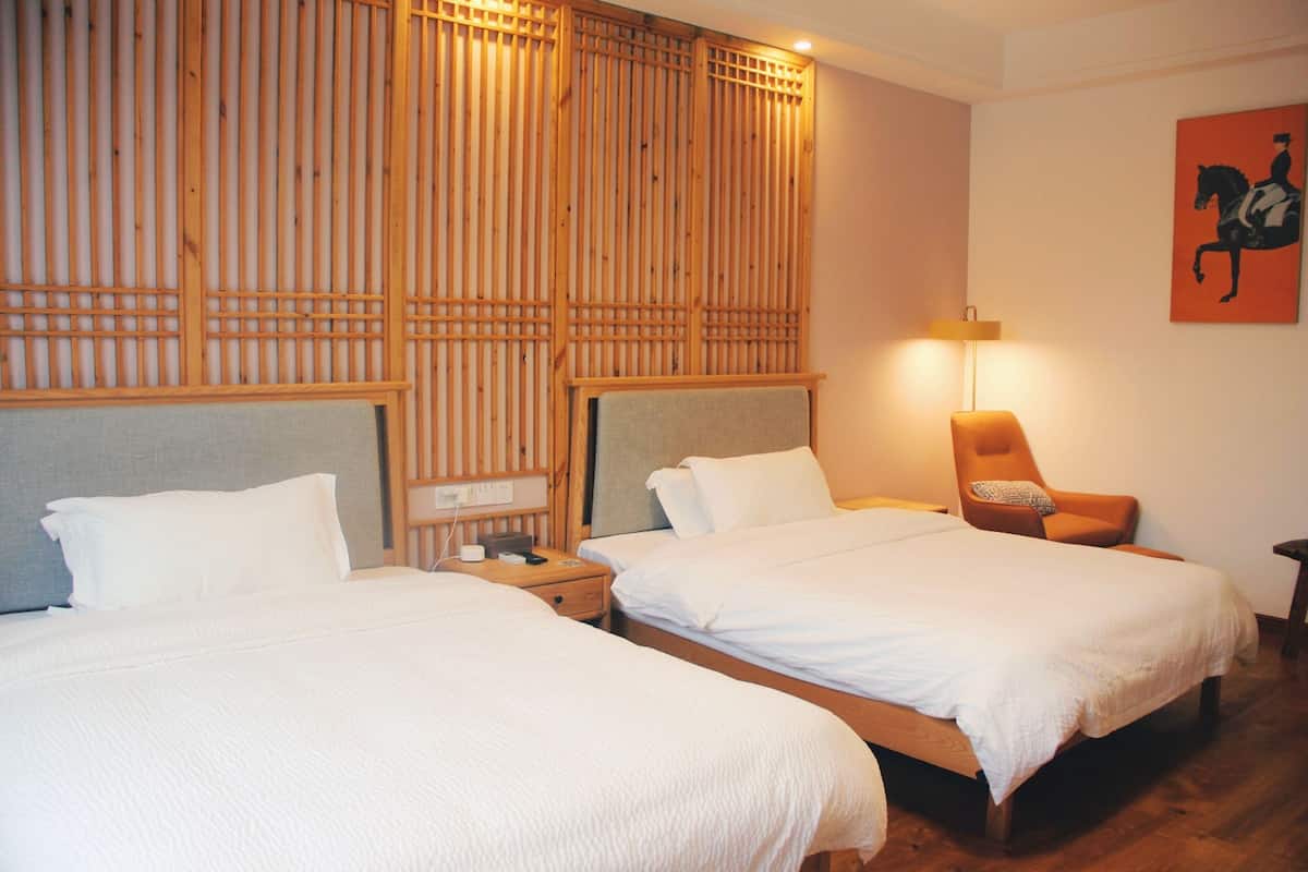 Een hotelkamer met twee bedden, houten hoofdeinden, een nachtkastje, een stoel, een lamp en een kunstwerk aan de muur.