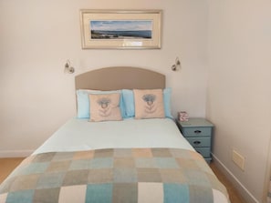 Quarto com cama, mesa de cabeceira, quadro na parede e manta xadrez.