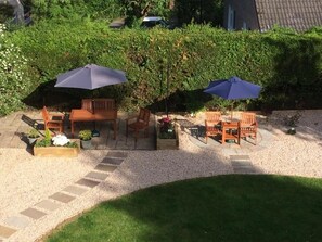 An outdoor seating area with wooden furniture and blue umbrellas, surrounded by a gravel path and a grassy lawn. - Fir Tree B&B at Galvelbeg House (Crieff)