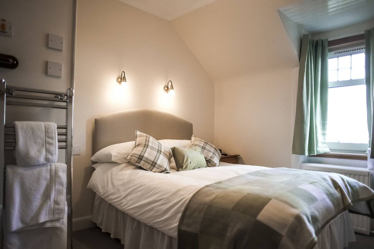 Une chambre à coucher comprenant un lit, deux lampes fixées au mur, une fenêtre avec des rideaux et un porte-serviettes.