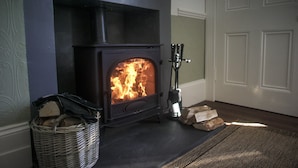 A wood-burning stove with logs and a basket of firewood. - Fir Tree B&B at Galvelbeg House (Crieff)