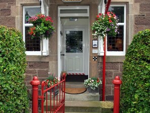A building entrance with a white door, red railings, and flower baskets on either side. - Fir Tree B&B at Galvelbeg House (Crieff)