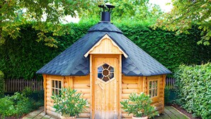 Eine Holzhütte mit einer sechseckigen Tür, einem Schornstein und Blumentöpfen am Eingang.