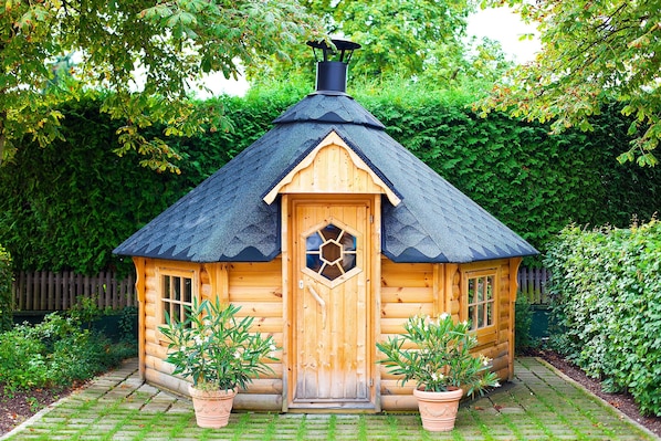 A wooden cabin with a hexagonal door, a chimney, and potted plants at the entrance.