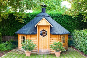 Una cabaña de madera con una puerta hexagonal, una chimenea y plantas en macetas en la entrada.