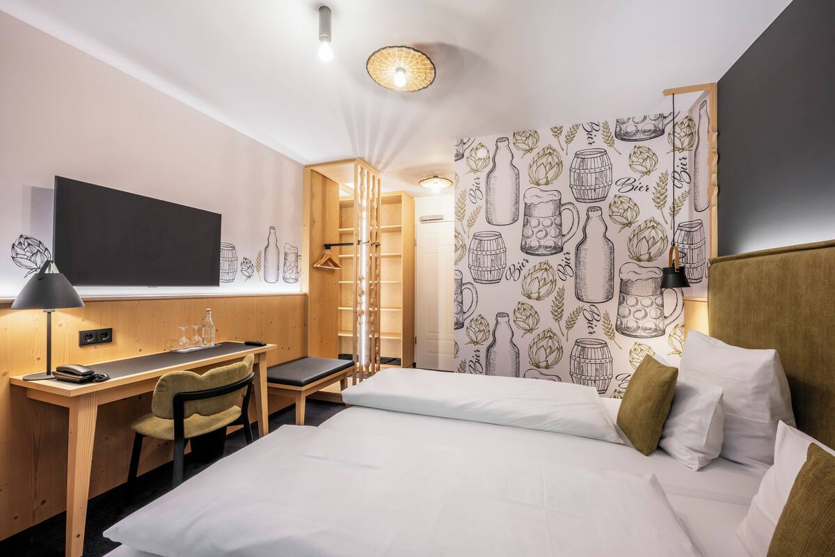 Camera d'albergo con un letto, una scrivania, una sedia, una TV e carta da parati a tema birra.