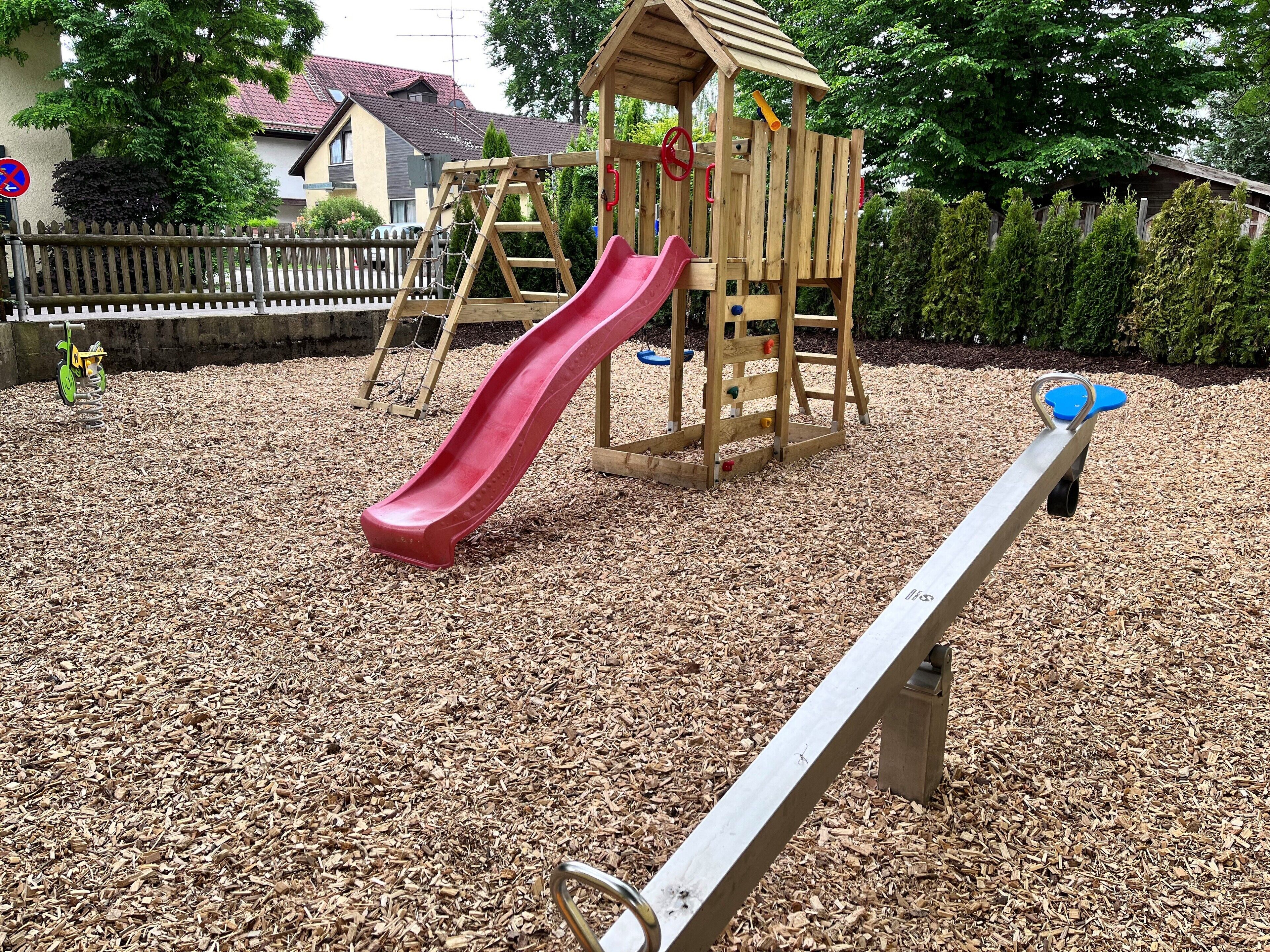 A playground with a red slide, a seesaw, and a wooden climbing structure.