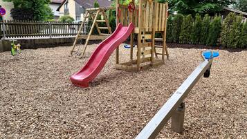 A playground with a red slide, a seesaw, and a wooden climbing structure.