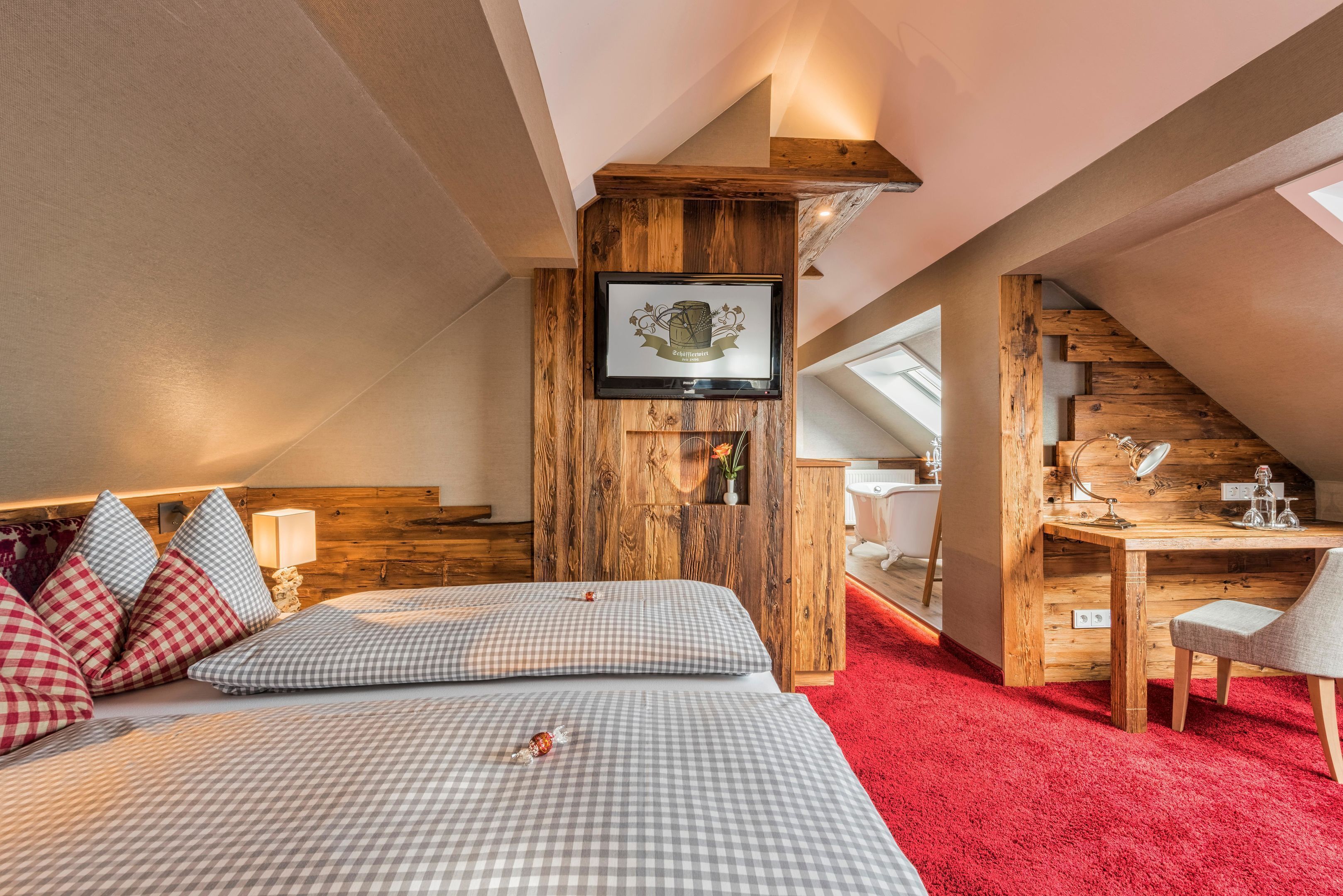 Un dormitorio con cama, ropa de cama a cuadros, cabecera de madera, escritorio con silla y espejo.