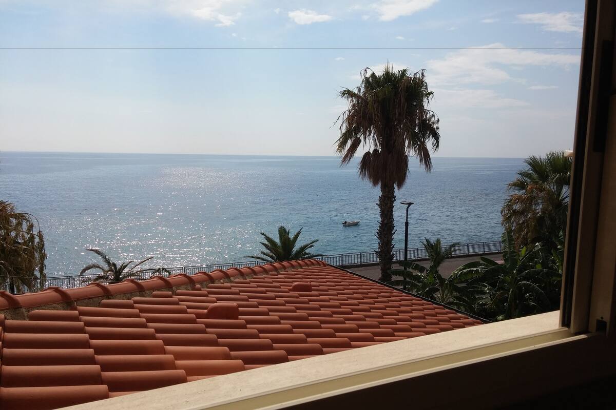 A view of the sea from a window with a tiled roof.