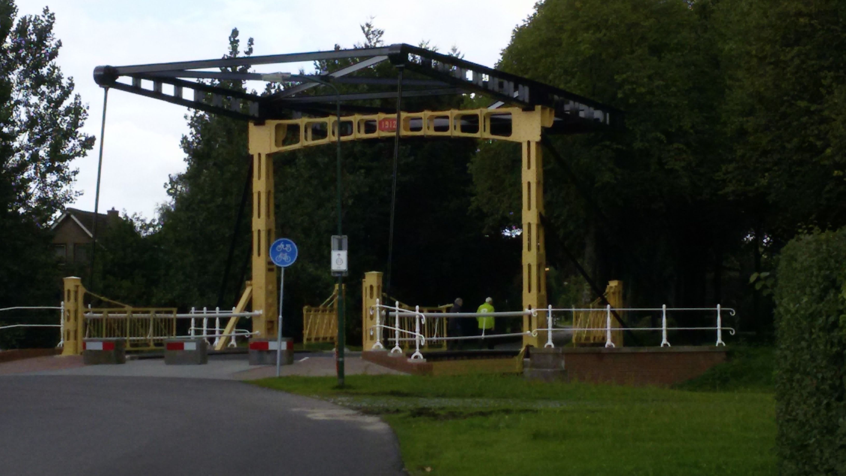 A pedestrian bridge with a metal structure and a blue sign indicating a bicycle path.