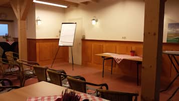 Un salón de conferencias con una pizarra, paneles de madera, sillas de mimbre, una mesa con mantel a cuadros y un cartel en la pared.