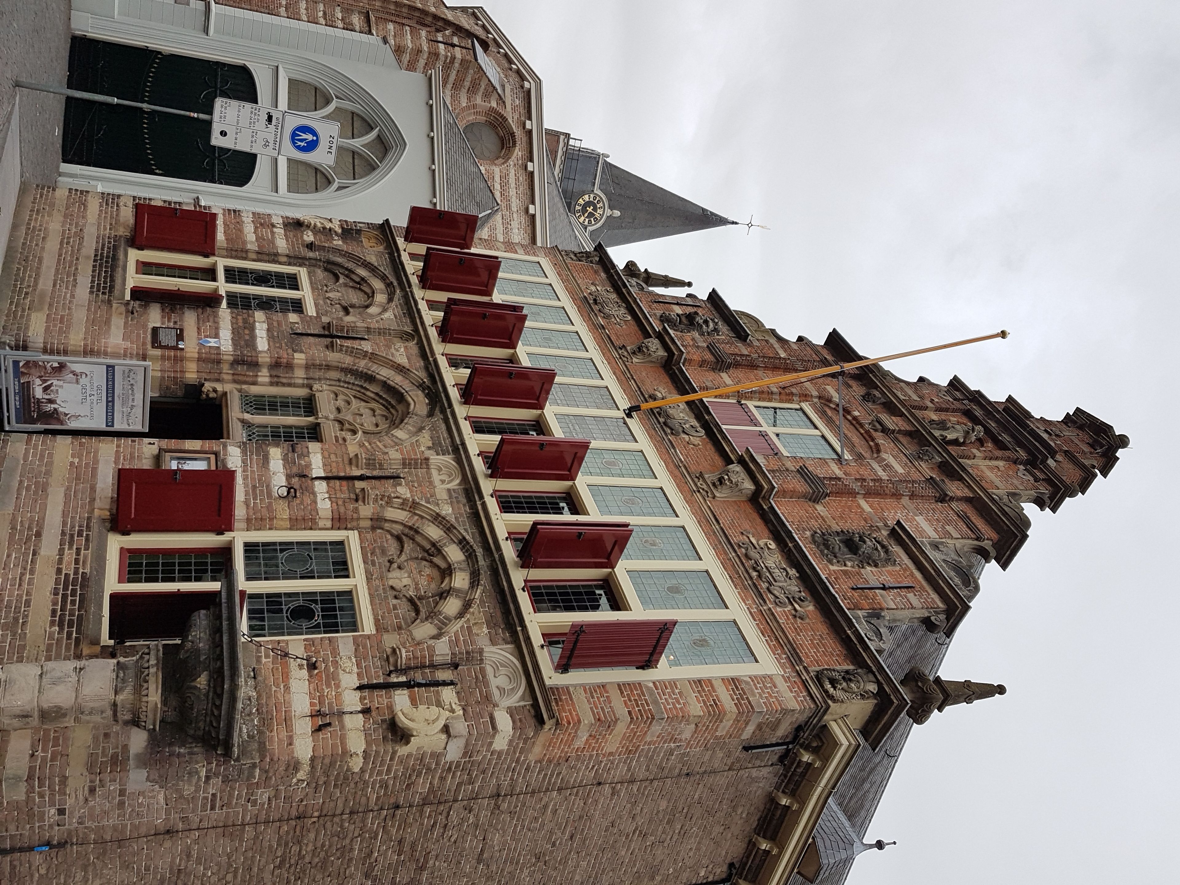 A historic building with a steeply pitched roof, ornate brickwork, and red window shutters.