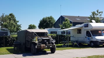 A military-style vehicle parked in a residential area with a large RV and a house in the background.