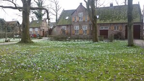 A traditional European-style building with a brick facade and multiple windows, surrounded by a lush garden with white and purple flowers. - Boerderij Hazenveld (Kockengen)