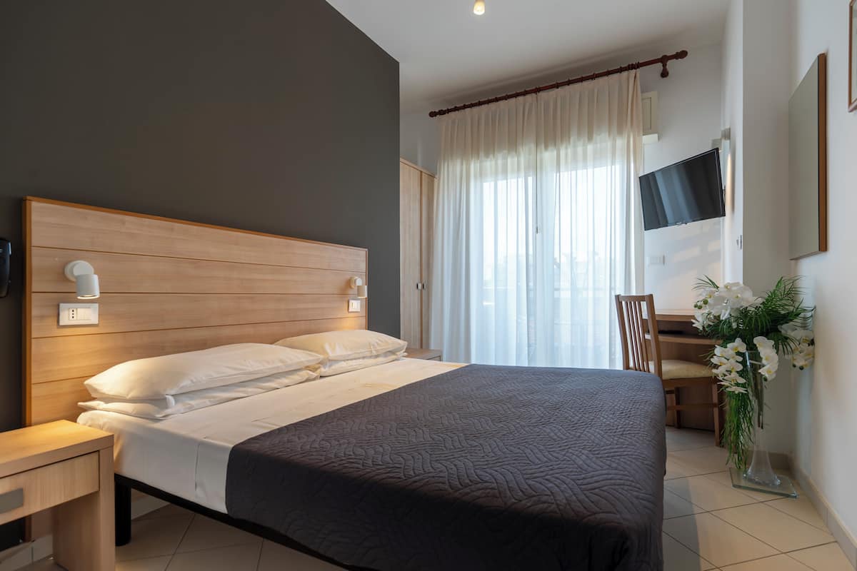 Une chambre d’hôtel comprenant un lit, une table de chevet, une télévision, une chaise, un bureau et une plante en pot.