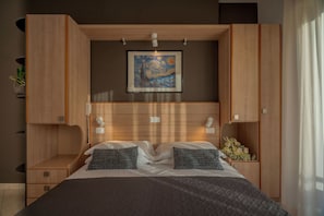 A modern bedroom with a wooden headboard, a painting above the bed, and a bedside table with a lamp.